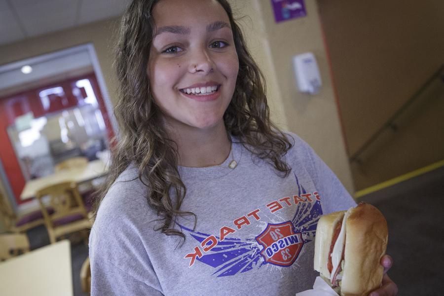 A student smiles while holding a sandwich.