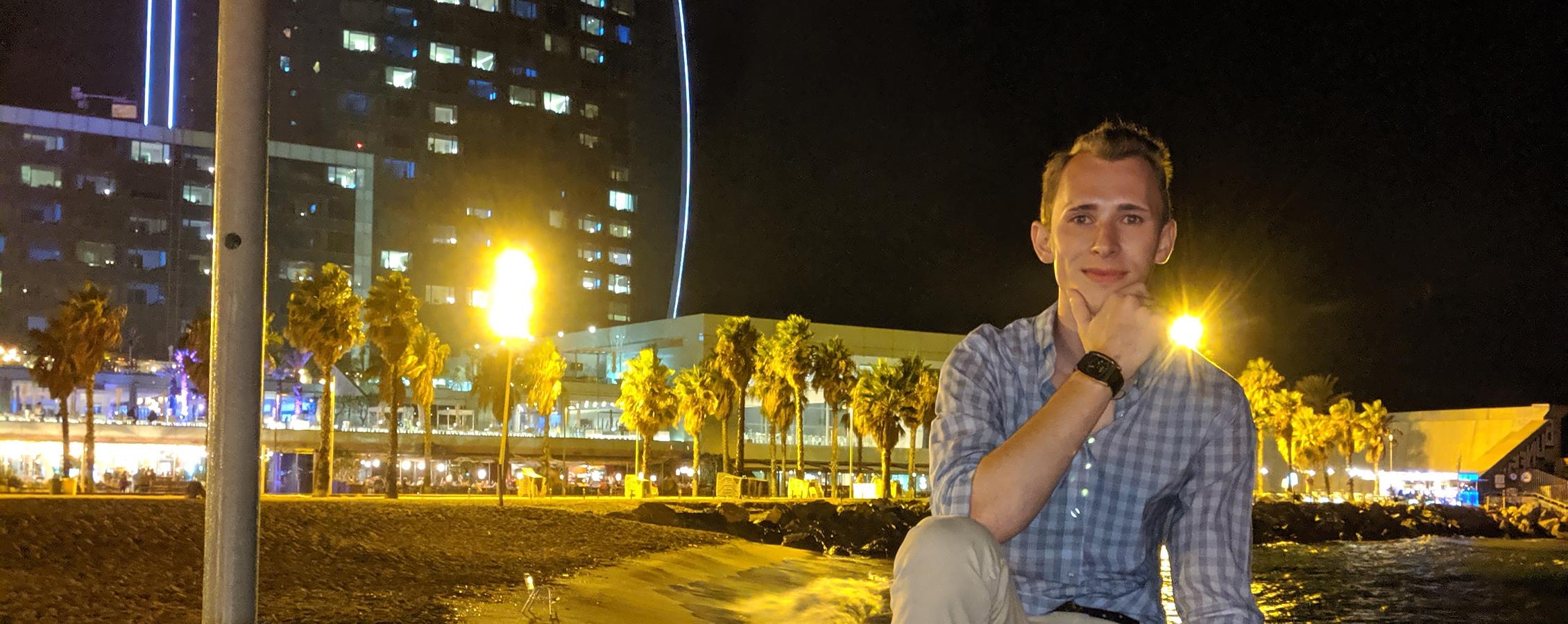 A person smiles at the camera with city lights behind them.