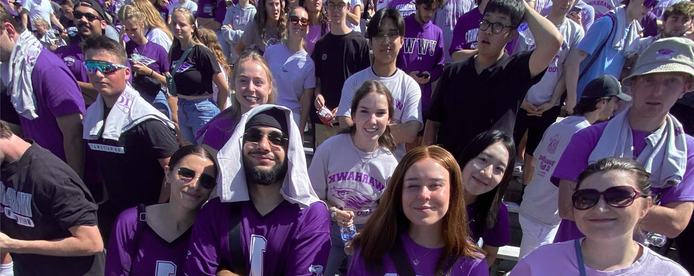 A group of international students pose for a photo while in the stands at Perkins Stadium watching a football game.