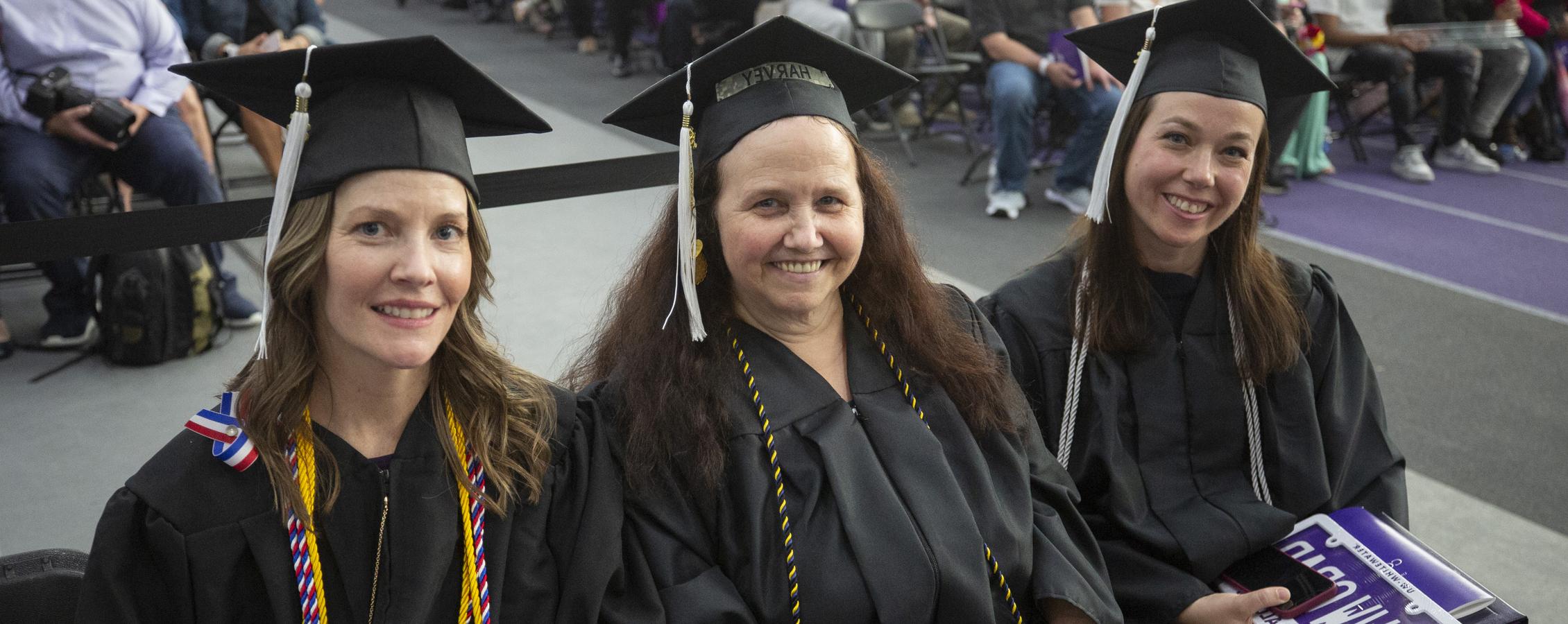 Three adult students wear their cap and gown at graduation.